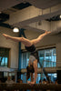 A gymnast balances in a handstand on the beam.