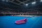 Purple tuba in the middle of gymnastics floor mat inside of an empty staduim.
