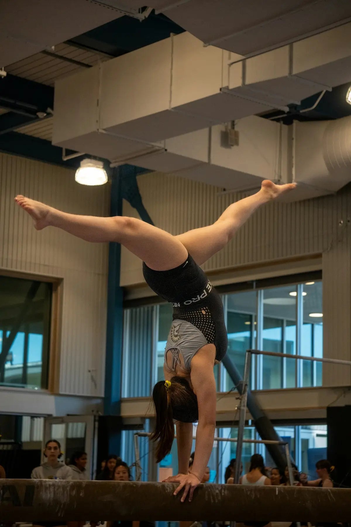 Back of a black and gray leotard with white lettering and a logo perfect for women’s gymnastics competitions and rhythmic gymnastics