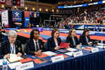Five judges in dark blazers scoring a women’s gymnastics floor routine with focus on gymnastics floor music.