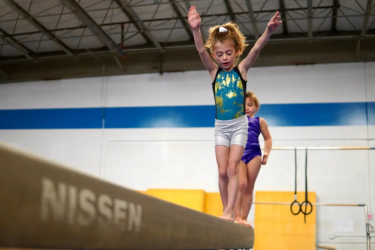 A young girl in a teal and gold sparkly leotard stands poised on a balance beam mastering flawless floor performance with gymnastics floor music